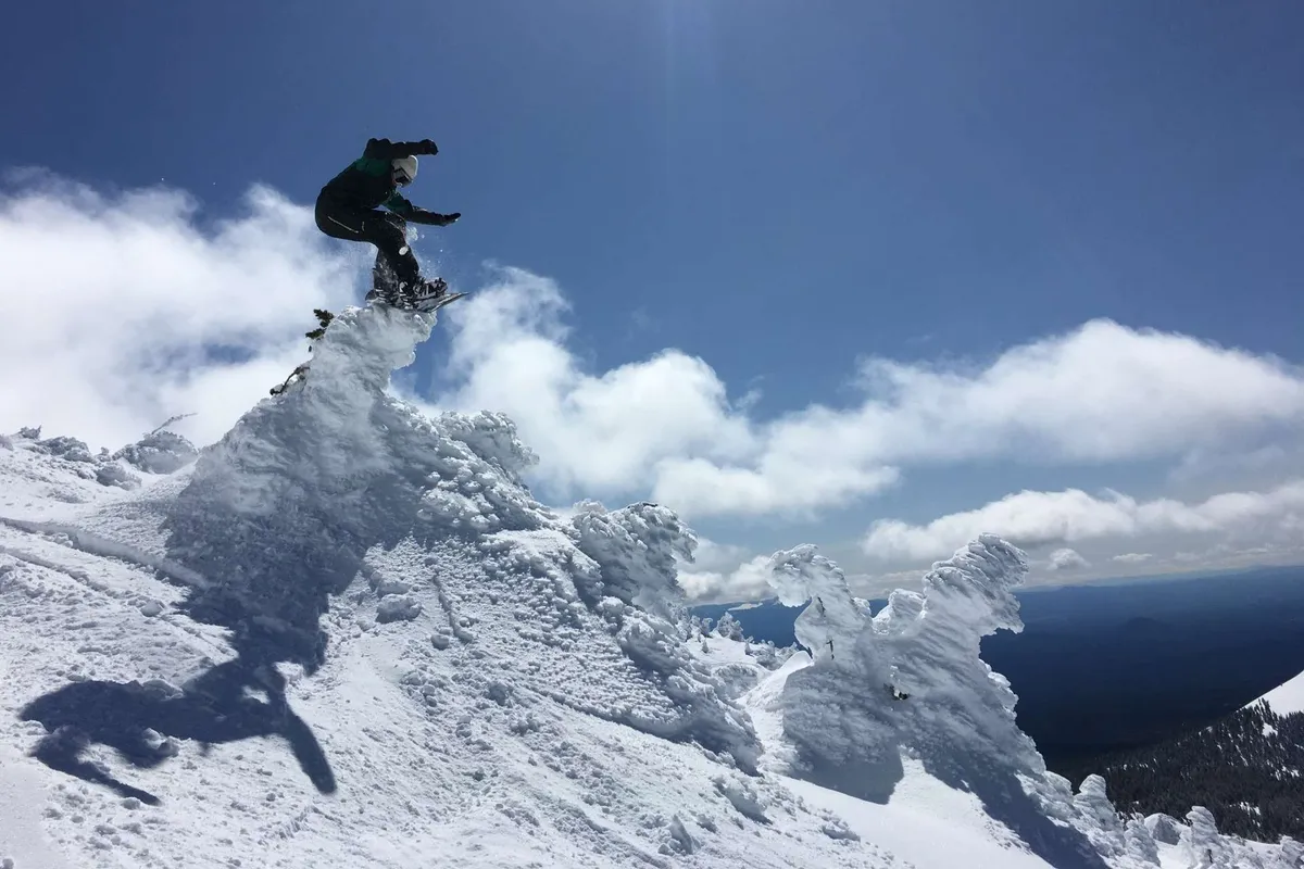 An exhilarating exterior scene featuring a snowboarder in mid-air against a dramatic backdrop of a snow-covered mountain peak and a sky filled with dynamic clouds. The image captures the thrill of outdoor mountain activities and the pristine beauty of the surrounding landscape, evoking a sense of adventure and escape.
