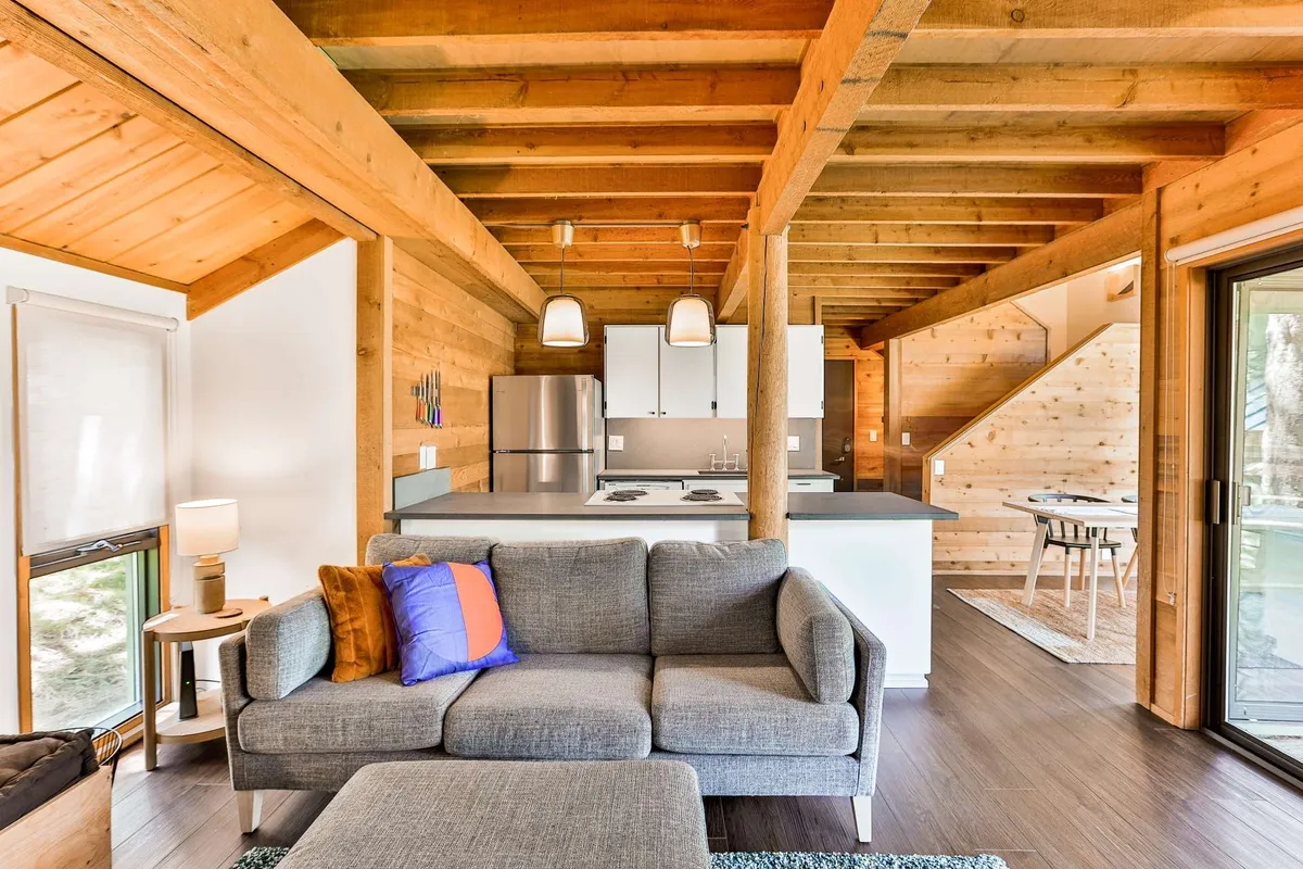 A welcoming, open-concept interior with a comfortable sofa at the center, kitchen island behind, staircase, and dining area visible. The arrangement encourages family interaction, with ample seating and space for various activities.