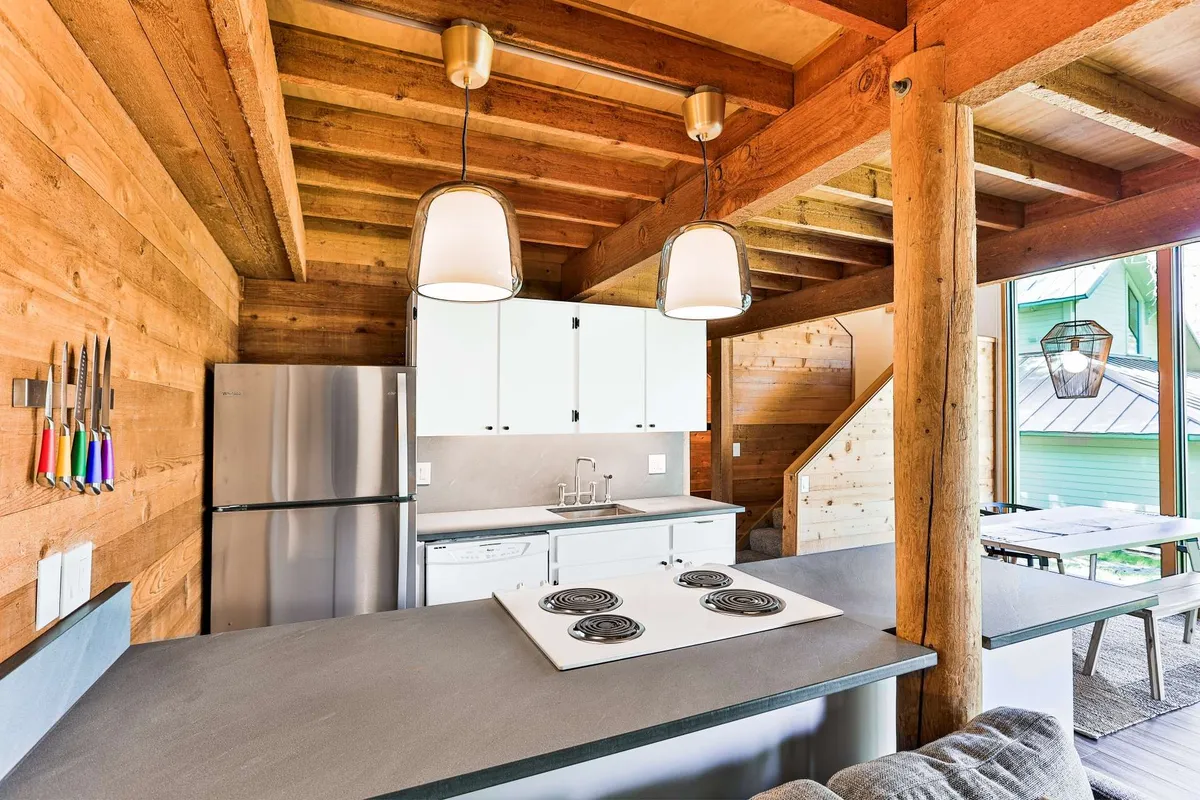 A stylish kitchen with a central island, stainless steel appliances, wooden beams overhead, and hanging light fixtures. The contemporary setup is inviting and designed for both cooking and entertaining, with ample seating around the island.