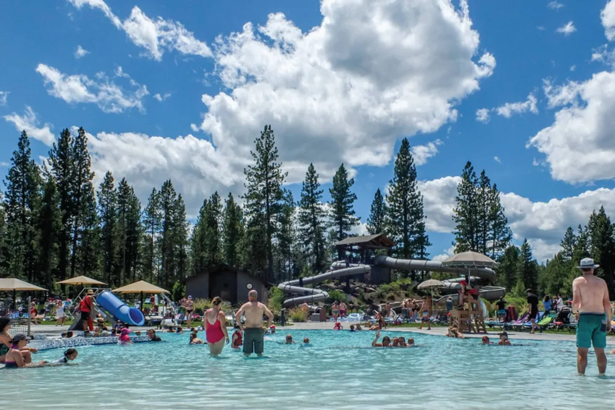 A lively exterior pool scene featuring a large swimming pool, an exciting water slide, and families enjoying the water. The atmosphere is joyful, highlighting fun and relaxation under the sun.